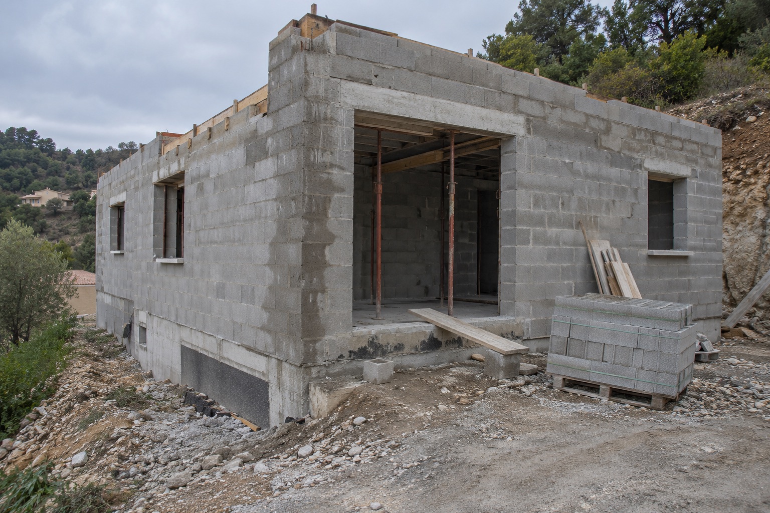Villa en cours de construction sur un terrain en pente, avec murs maçonnés et étaiement